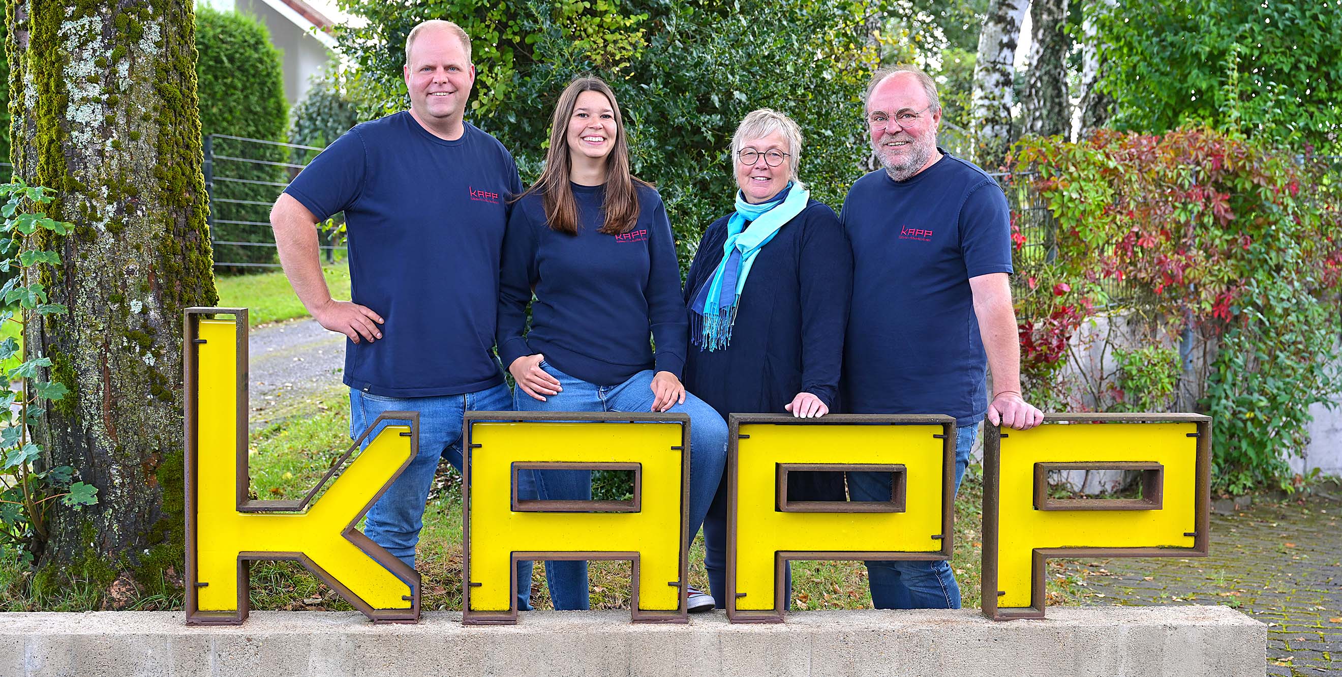 Foto: Familienunternehmen KAPP in Gehlert. Elsabe und Gunnar Giese sowie Tabea und Konstantin Giese stehen hinter dem Firmenschild, das in gelben Buchstaben KAPP zeigt.